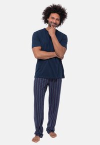 Sotilaskilpinen lyhythihainen t-paita yhdistettynä monivärisiin raidallisiin pyjamahousuihin. Kangas näyttää pehmeältä; housuissa on rento istuvuus ja joustava vyötärö.