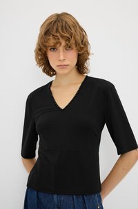 Sort V-hals T-shirt med 3/4 ærmer, der har perle accenter langs halsudskæringen. Lavet af glat, let stof.