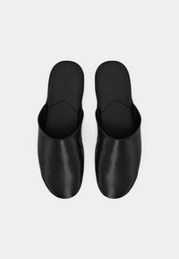 Par de pantufas de couro pretas, tipo slip-on, com a parte da frente fechada e as costas abertas, de design minimalista, exibidas sobre fundo branco.