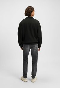 Felpa nera con polsini e orlo a coste, abbinata a jeans grigio scuro. Modello visto di spalle, con sneakers di colore chiaro.