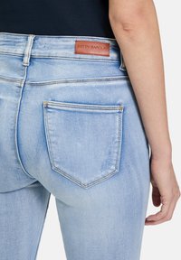 Jasnoniebieskie dżinsy z denimu z skórzaną naszywką oznaczoną "BETTY BARCLAY" przy pasku oraz dwiema tylnymi kieszeniami z widocznym przeszyciem.