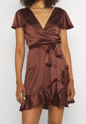 Frau trägt ein kurzärmeliges Satin-Wickelkleid in Dunkelbraun mit volantsaum und gebundenem Taillengürtel, kombiniert mit einer zarten Halskette.