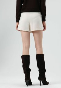 Witte op maat gemaakte shorts met een gladde textuur, voorzien van zijzakken. Gecombineerd met kniehoge zwarte suède laarzen met een stilettohak.