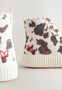 Canvas enkelboots in het wit met een zwart en bruin koeienprint, voorzien van een rood geborduurd hartdetail en een gestructureerde witte rubberen zool.
