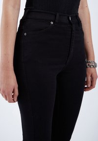 Vaqueros de tiro alto negros, confeccionados en denim elástico, que presentan un ajuste slim, costuras sutiles y detalles metálicos en los bolsillos.