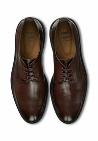 Brązowe skórzane buty o gładkim wykończeniu, z zapięciem na sznurowadła i zaokrąglonym noskiem. Posiadają subtelne przeszycia oraz wyściełane wnętrze.