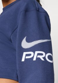 Felpa cropped blu navy in misto cotone, con logo Nike bianco e testo "PRO" sulla manica destra. Texture liscia.