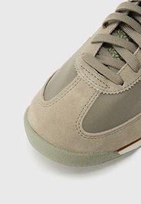 But ze zamszu oliwkowego i siateczki, z teksturowanymi akcentami, zaokrąglonym noskiem i płaskimi beżowymi sznurowadłami. Widoczna gumowa podeszwa.