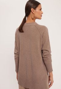 Brązowy, teksturowany sweter z dzianiny o luźnym kroju, z prążkowanymi mankietami i dołem oraz nieco dłuższym tyłem. Subtelne detale szwu na ramionach.