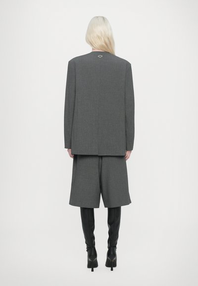 Blazer grigio su misura con pantaloni corti larghi coordinati, tessuto texture e un piccolo accento di diamante sul retro, abbinato a stivali neri sopra il ginocchio.