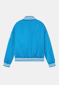 Ljusblå bomberjacka med vitrandig ribbad krage, ärmar och midjeband, visad bakifrån på en vit bakgrund.