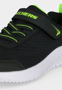Chaussure de sport Skechers noire et vert néon avec tige en mesh, bride velcro, lacets élastiques et semelle blanche texturée.