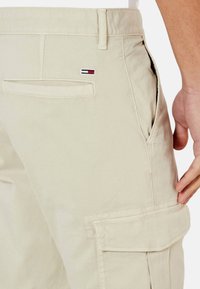Pantalones cargo caqui con bolsillos laterales, un bolsillo trasero de parches y el logotipo de la marca bordado en rojo, blanco y azul en el bolsillo trasero. Textura suave.