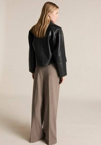 Veste en cuir noir courte avec un large col, associée à un pantalon beige à jambes larges. Texture lisse et design structuré avec un minimum de détails.