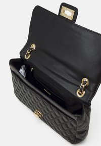 Černá prošívaná kabelka z kůže se zlatým kováním. Má prostorný interiér a kapsu pro uspořádání.