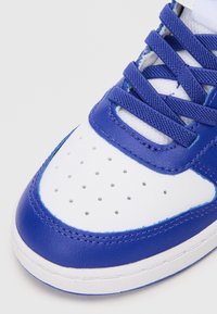 Tenis com uma base de couro branco e detalhes em couro azul. Apresenta biqueira perfurada, atacadores texturizados e sola de borracha.
