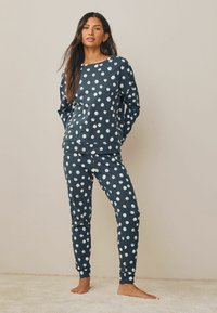 Mörkblå pyjamas set i mjukt tyg, med ett prickigt mönster med vita cirklar. Toppdelen har rund halsringning, och byxorna har uppvikta ankle.