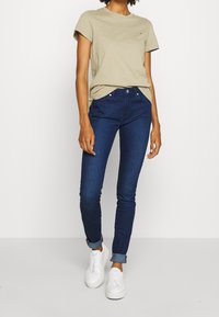 Vaaleanbeige puuvillapaita, jossa on lyhyet hihat, yhdistettynä tummansinihin slim fit -farkkuihin. Valkoiset lenkkarit viimeistelevät ilmeen. Yksinkertainen ja rento asu.