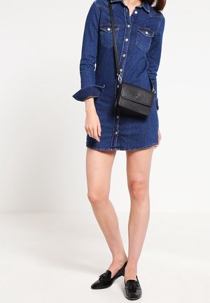 Černá kožená kabelka přes rameno s klopou a stříbrným kováním; nošena s modrými denimovými šaty a černými mokasíny.