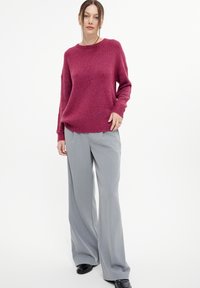 Maglione fucsia a maglia con scollatura rotonda e maniche lunghe, abbinato a pantaloni a vita alta e gamba larga di colore grigio chiaro. Scarpe nere.