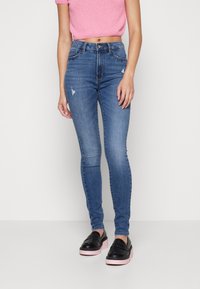 Mujer vestida con jeans ajustados de tiro alto en azul con ligeras desgastaciones, un suéter de punto rosa recortado y mocasines de plataforma negros con suelas rosas.