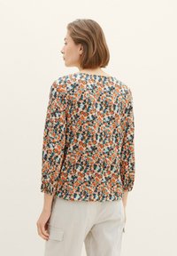 Blumenbluse mit dreiviertel Ärmel, versehen mit einem orangefarbenen, blauen und weißen Druck. Leichter Stoff, runder Ausschnitt und geraffte Manschetten.