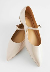 Ballerines Mary Jane en cuir verni beige avec un bout pointu, une sangle et un détail de boucle, et une doublure intérieure lisse, offrant un design élégant.
