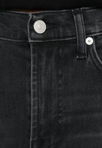 Vaqueros negros de denim con cintura estándar, cierre de botón metálico, diseño de cinco bolsillos y acabado con textura suave.