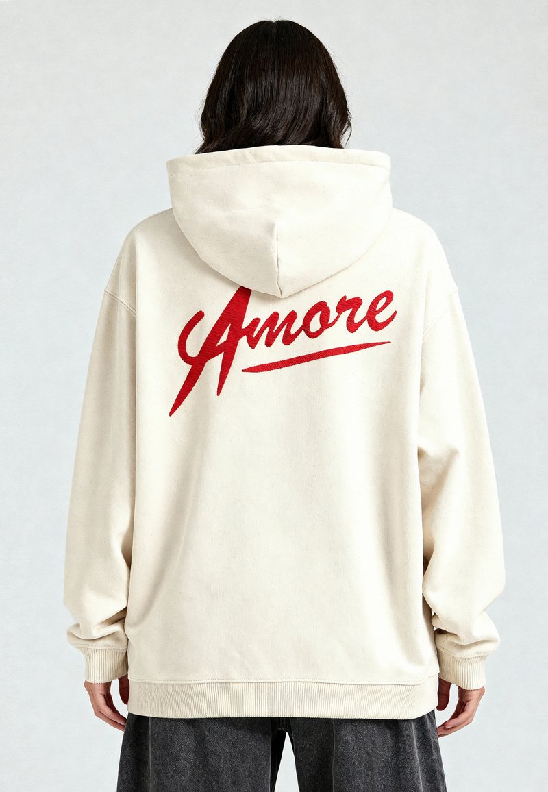 Kreemikas kapuutsiga särk, mille seljal on punane "Amore" graafika, valmistatud pehmest kangast, millel on lõdva lõike ja soonikkudega varrukad.