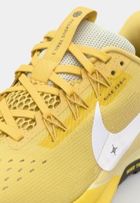 Les baskets Nike Pegasus Trail 5 présentent un dessus jaune avec des accents en mesh, des détails texturés et un logo swoosh blanc. Les lacets sont jaunes.