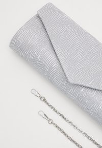Srebrna kopertówka z teksturowanym wzorem fal. Posiada kopertowy design i zawiera dwa srebrne łańcuszki do noszenia.