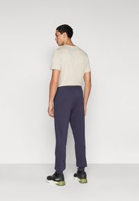 Σκούρο μπλε φόρμα με ελαστική μέση, πλαϊνές τσέπες, συνδυασμένη με ανοιχτό μπεζ μπλουζάκι και μαύρα αθλητικά παπούτσια με πράσινες λεπτομέρειες.