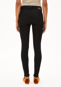 Jeans ajustados negros de mezclilla, con una cintura alta, dos bolsillos traseros y un ajuste ceñido a lo largo de las piernas.