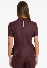 Burgunderfarbige Bluse mit kurzen Ärmeln, vertikalem Streifenmuster, einem peplumartigen Saum und einem Schlüssellochausschnitt hinten mit zwei schwarzen Knöpfen. Glatte Textur.