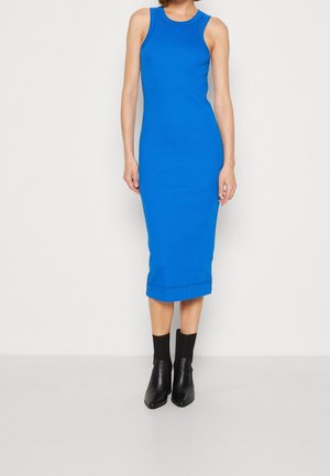 Bezrękawnik, jasnoniebieska sukienka midi z okrągłym dekoltem, noszona z czarnymi botkami i skarpetkami na stojącej osobie.