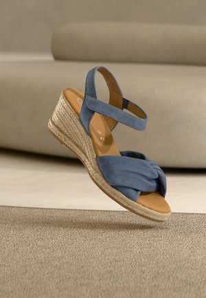 Blue suede wedge sandal with knotted front strap and woven rope platform sole, displayed against a beige background.