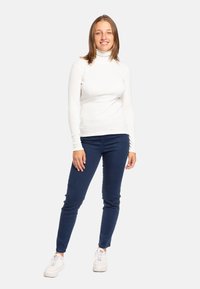 Maglione a collo alto bianco a maniche lunghe, aderente; abbinato a jeans skinny blu scuro e sneaker bianche. Design semplice e tessuto elasticizzato.