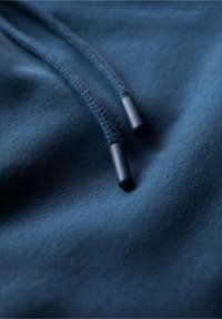 Mörkblå hoodie i tyg med en strukturerad yta, försett med två svarta dragsnören med plastspetsar. Närbild som framhäver materialdetaljer.