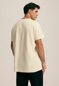 Beżowa bawełniana koszulka z okrągłym dekoltem, krótkimi rękawami i luźnym krojem, z gładką teksturą i prostym dołem.