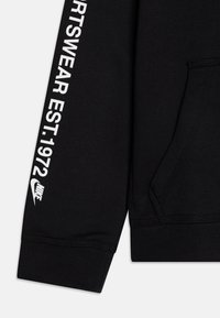 Black hoodie with a front pocket, featuring white text "SPORTSWEAR EST. 1972" along the sleeve and a Nike logo. Smooth fabric texture.