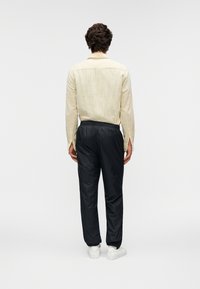 Κίτρινο υφασμάτινο πουκάμισο με μακριά μανίκια και καμπυλωτό γιακά, σε συνδυασμό με μαύρο παντελόνι  με ελαστική μέση και λευκά αθλητικά παπούτσια, από πίσω όψη.