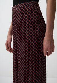 Wijde broekspijpen met een diamantpatroon in rood, zwart en blauw. Gemaakt van een zachte stof, met een gladde textuur en een op maat gemaakte tailleband.