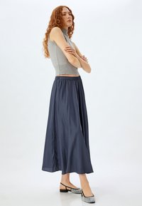 Haut sans manches gris avec texture côtelée et col montant, associé à une longue jupe fluide bleu marine foncé et des ballerines ornées.