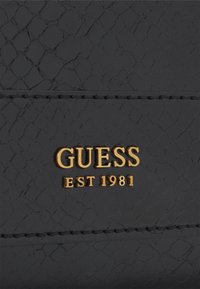 Sort tekstureret pung med et reptilmønster, der har et guld "GUESS" logo og "EST 1981" præget detalje. Glat syning langs kanterne.