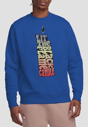 Royal blue sweatshirt featuring a large graphic of a candle with the text "LIT THE BLACK FLAME CANDLE" in multicolored, layered typography.