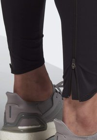 Black athletic leggings with a zip closure at the ankle, paired with grey running shoes featuring a textured mesh upper and cushioned sole.