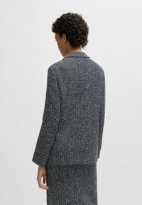 Navy blazer with a textured fabric containing flecks of white. Single-breasted design, notched collar, and long sleeves.