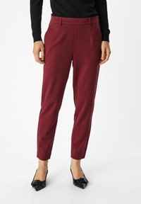 Pantalon fuselé bordeaux à texture lisse, avec poches avant et plis simples, associé à des escarpins noirs à bouts pointus.