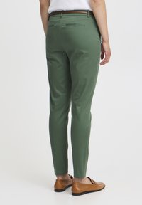 Pantalons verts en mélange de coton, design ajusté, avec deux poches à l'arrière. Associés à des mocassins marron, au fit classique.