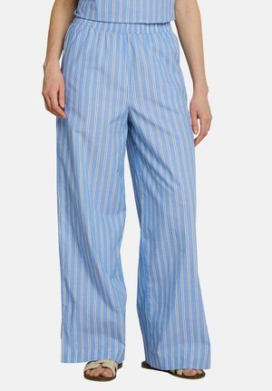 Pantalon large bleu clair avec des rayures verticales blanches et beige, porté avec des sandales beiges, vu de la taille aux pieds.